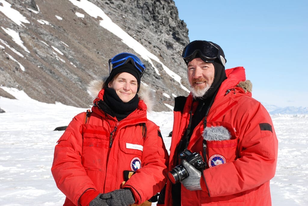 Two explorers in Antarctica wearing red parkas.