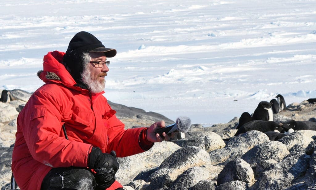 Man in red coat with penguins on icy landscape